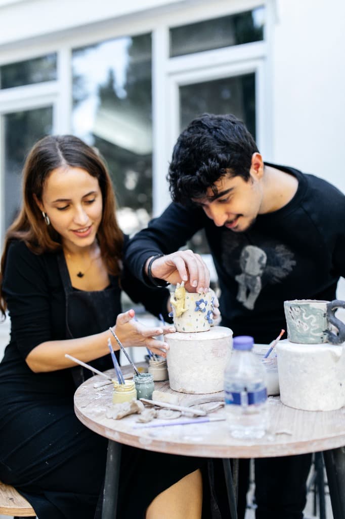 Two people shaping pottery together at a craft table